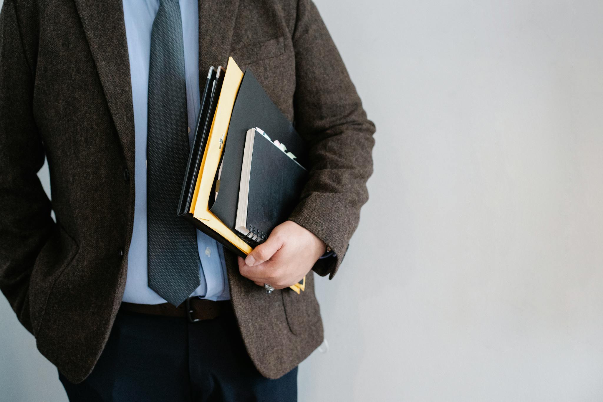 Business professional in a suit holding various folders and notebooks indoors.